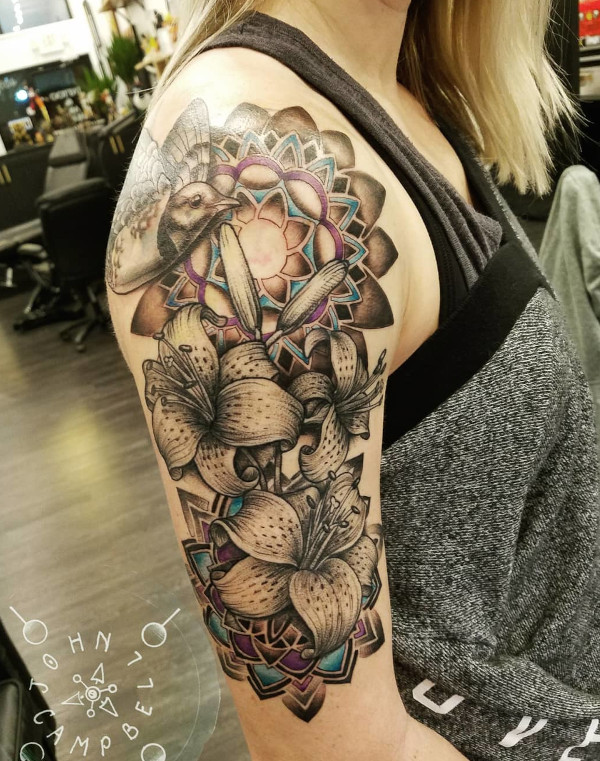 Black and grey with pops of color mandala and Lily upper arm tattoo with bird by John Campbell at Sacred Mandala Studio tattoo parlor in Durham, NC.